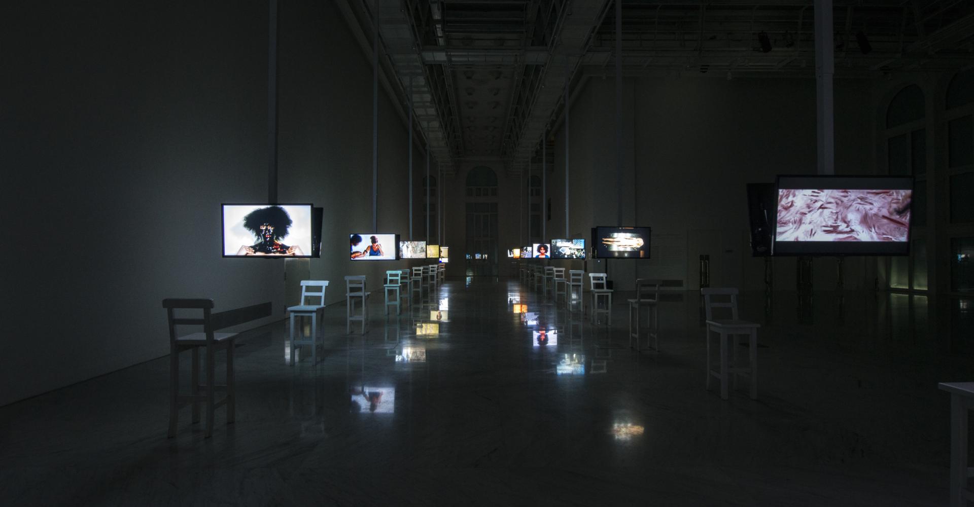 Two rows of televisions with photographs each with a single chair placed in front