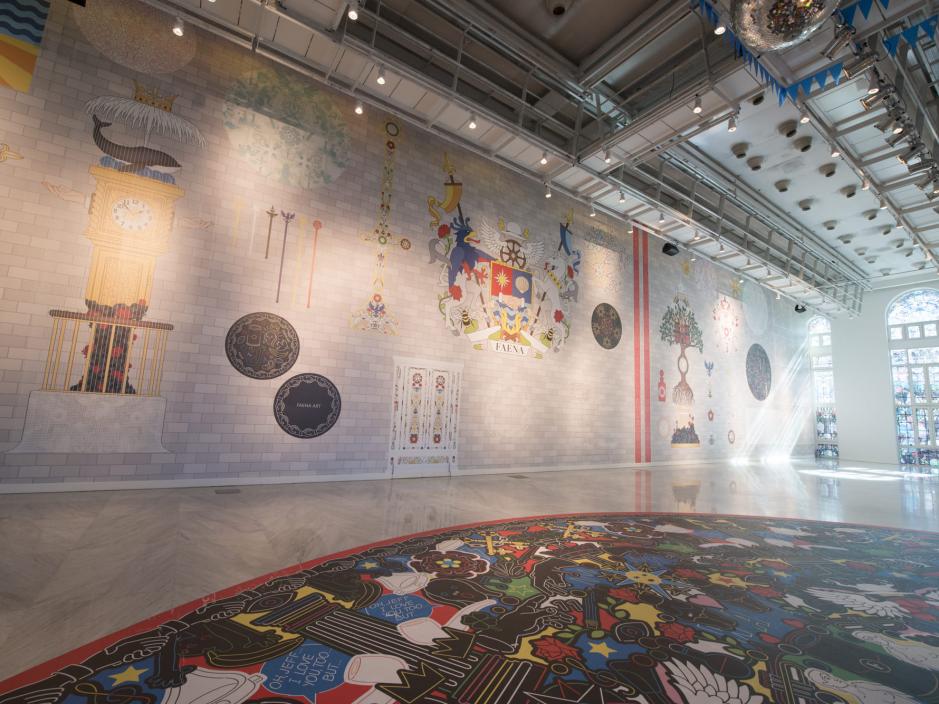 A room with murals along the wall and the floor with large stained glass windows