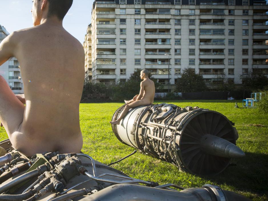 Nude men sitting on metal sculptures in a park