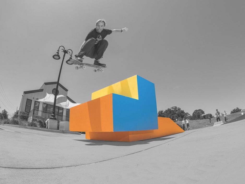 black and white photo of man jumping skateboard over colourful ramp