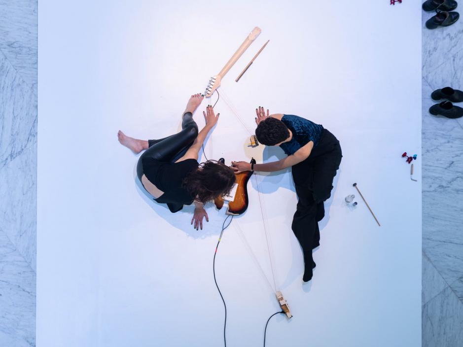 Two people on the floor playing a broken guitar