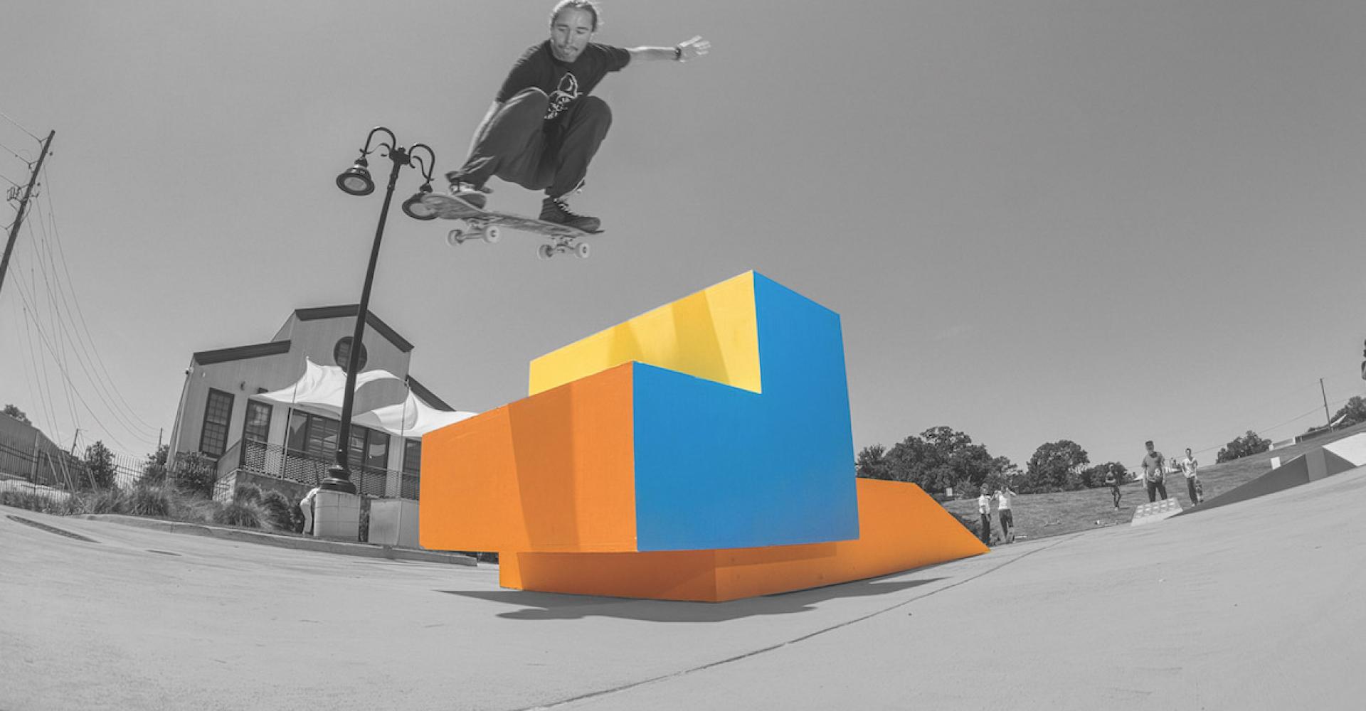 black and white photo of man jumping skateboard over colourful ramp