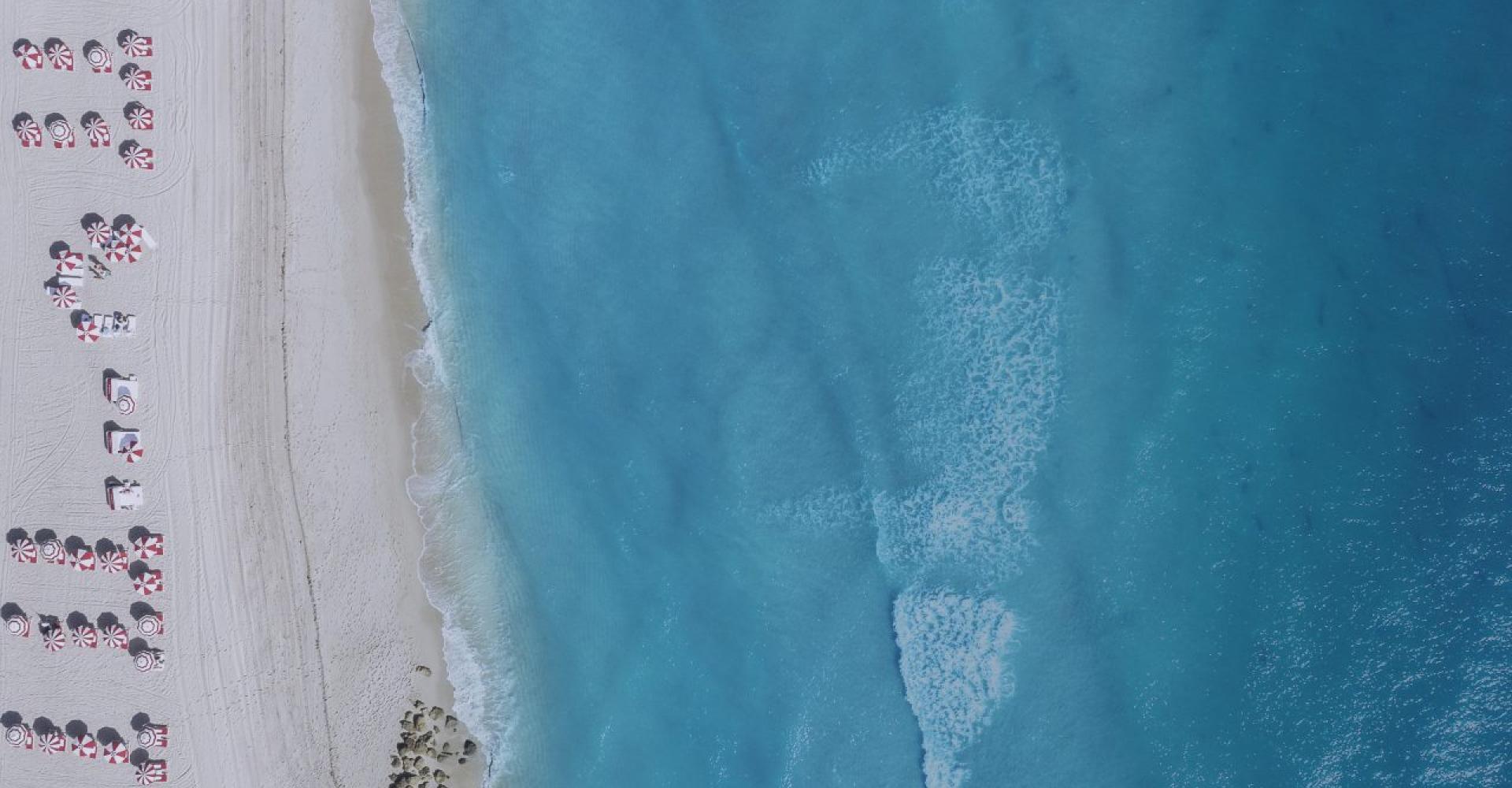 aerial view of blue ocean and white sand beach with red and white umbrellas